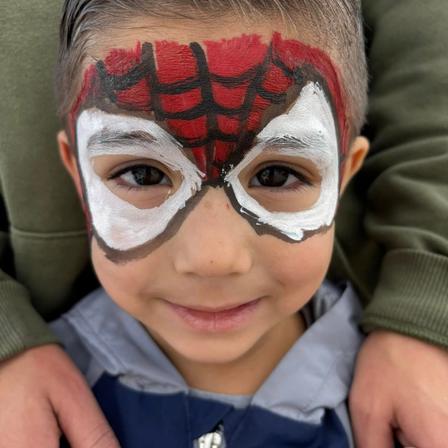 A smiling boy wearing a hand-painted red and white Spider-Man face design.